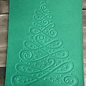 May include: A green card with an embossed design of a Christmas tree. The tree is made up of swirls and stars.