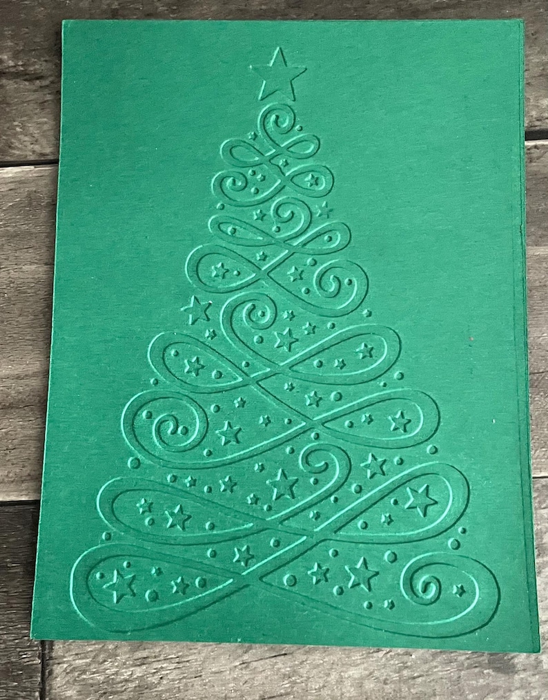 May include: A green card with an embossed design of a Christmas tree. The tree is made up of swirls and stars.