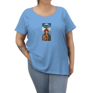 May include: A light blue women's t-shirt with a colorful illustration of a woman with a fishtail on her head holding a red rose.