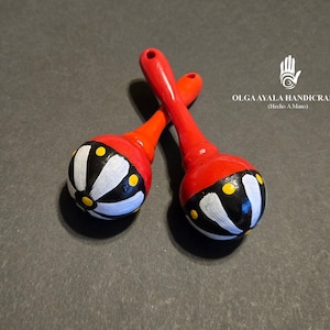 May include: Two red wooden maracas with black and white painted designs. The maracas have yellow accents and a white flower design.