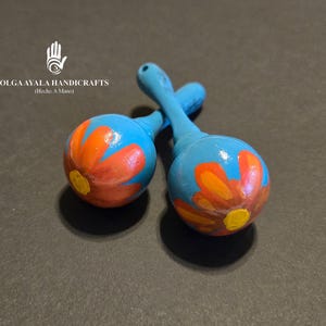 May include: Two blue maracas with orange and yellow flower designs. The maracas are handmade and have a hand-painted design.