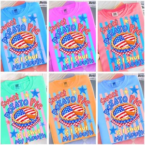 May include: A collection of crew neck t-shirts in various colors, each featuring a graphic of a sweet potato pie with an American flag design. The text reads "Sweet Potato Pie & I Shut My Mouth".