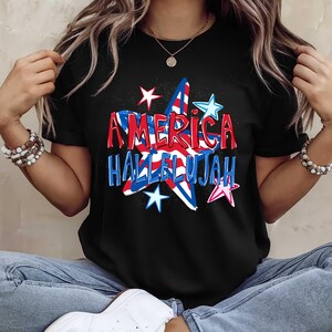 May include: Black t-shirt featuring a patriotic design with the words "AMERICA HALLELUJAH" in red and blue, set within a star shape. Additional stars in various colors surround the text.