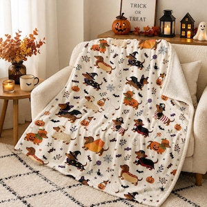 Peut inclure: Un plaid de couleur crème orné d'un motif répétitif de teckels portant divers costumes d'Halloween, notamment des citrouilles, des fantômes et des chapeaux de sorcière, parsemé de petites araignées, de toiles, de chauves-souris et de bonbons.