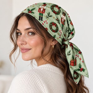May include: A sage green headscarf featuring a repeating Christmas pattern of nutcrackers, holly leaves with red berries, candy canes, and wrapped gift boxes. The fabric is tied at the back with two triangular ends hanging down.