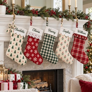 May include: Five personalised Christmas stockings hanging in a row. The stockings feature names Charlotte, Olivia, Henry, Sophie, and William embroidered on white cuffs. Patterns include green trees, white snowflakes, green plaid, red berries, and red plaid.
