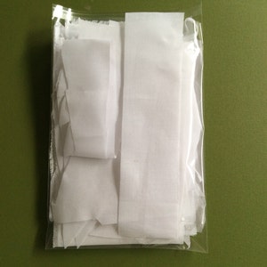 May include: A clear plastic bag filled with white fabric scraps. The fabric is cut into various shapes and sizes.