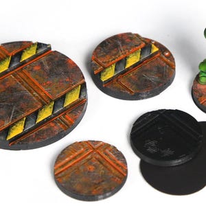 May include: Set of six round miniature bases for tabletop gaming.  Four bases feature a rusty metal texture with yellow and black warning stripes. Two bases are black with a textured surface.