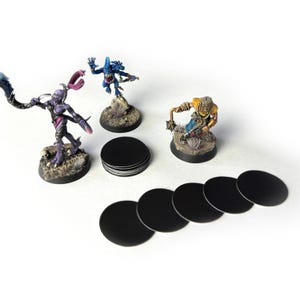 May include: A set of 10 black round bases for miniature figures, along with three painted miniature figures on bases. The figures are a blue and purple creature, a yellow and brown creature, and a purple creature with a long tail.