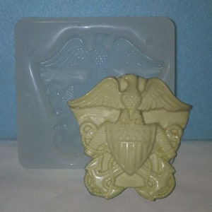 May include: A white silicone mold for making a resin casting of the United States Navy emblem. The emblem features an eagle with outstretched wings, a shield with stars and stripes, and two crossed anchors.