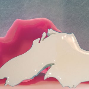 May include: A pink silicone mold of the outline of a lake, with a white resin casting of the lake inside the mold.