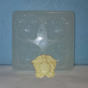 May include: A clear, rectangular mold with four eagle crest impressions and a finished cream-colored eagle crest. The eagle crest features a shield, wings, and other details. The mold is made of a flexible material.