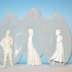 May include: A clear, flexible silicone mold with three white figurines: a man in a winter outfit and two women in long dresses. The mold has a wavy shape. The figurines are unpainted and stand on a light blue surface.
