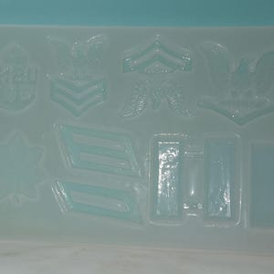 May include: A clear silicone mold with various shapes, including stars, eagles, and military insignia. The mold is designed for creating decorative items or cake toppers.