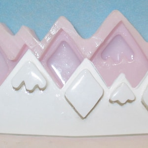 May include: Pink silicone mold shaped like a mountain range with five peaks. The mold has a white base and is designed for making cake decorations.