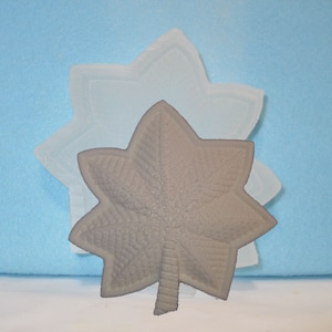 May include: A gray silicone mold of a five-pointed star with a detailed leaf design. The mold is used to create a decorative star for crafts or cake decorating.