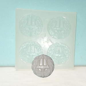 May include: A clear silicone mold with four circular impressions and a single, detached, gray, circular emblem. The emblem features a trident design within a wreath. The mold is for creating decorative elements.