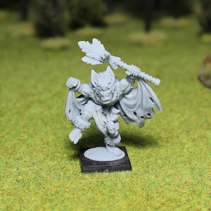 Puede incluir: Una figura en miniatura gris de una criatura parecida a un murciélago con un bastón y una capa hecha jirones. La figura está sobre una base cuadrada negra, con una cara detallada y texturas similares a la piel. El fondo es verde.