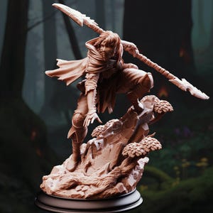 Puede incluir: Figura detallada de un guerrero en pose dinámica, sosteniendo una lanza con una hoja dentada. La figura está vestida con una capa con capucha y está colocada sobre una base rocosa con árboles en miniatura. El color es un tono cálido y terroso.
