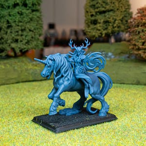 Peut inclure: Une figurine miniature monochrome bleue représentant un cavalier aux grands bois monté sur une licorne. La figurine est placée sur une base rectangulaire noire, avec des détails sculptés complexes sur la crinière, la queue et la tenue.