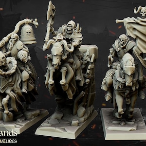 Op de afbeelding: Drie gedetailleerde miniatuurbeeldjes van skeletkrijgers die op skeletpaarden rijden. De figuren zijn lichtgrijs van kleur en zijn gemonteerd op rechthoekige bases. Eén figuur houdt een spandoek vast, een ander een bijl en de derde een bel.