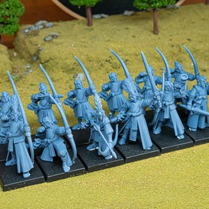 Puede incluir: Un grupo de figuras en miniatura azules de arqueros y espadachines. Las figuras están dispuestas sobre una base negra, algunas con arcos y flechas, otras con espadas. El fondo presenta un terreno verde y marrón.