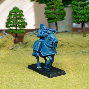 Peut inclure: Une figurine miniature en plastique bleu représentant un chevalier en armure monté sur un cheval, fixée sur un socle rectangulaire noir. Le chevalier tient un grand marteau sur l'épaule et le cheval porte un harnachement de protection.