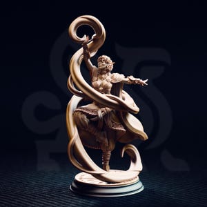 Puede incluir: Figura beige de una mujer con un vestido fluido, con los brazos extendidos, con un elemento en forma de cinta arremolinada. La figura está sobre una base redonda, sobre un fondo oscuro.