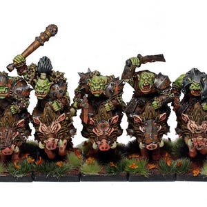Könnte beinhalten: Miniaturfiguren von grünschlägigen Orks, die auf braunen Kriegswildschweinen reiten, bewaffnet mit Waffen und Rüstungen. Die Orks sind in einer kampfbereiten Haltung mit einem Knüppel und Schwertern dargestellt. Die Figuren stehen auf einer grasbewachsenen Basis.