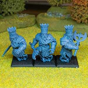 Puede incluir: Tres figuras en miniatura de plástico azul sin pintar sobre bases cuadradas negras. Cada figura lleva una corona y armadura con túnicas fluidas, y sostiene un hacha. Las figuras tienen un aspecto espectral con cuerpos inferiores arremolinados.