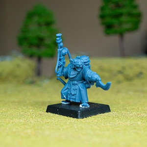 Puede incluir: Una figura miniatura de plástico azul de un guerrero rata antropomórfico sobre una base cuadrada negra. La figura viste una túnica larga, lleva una mochila y sostiene un arma de fuego de cañón largo y una hoja curva en las manos.