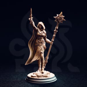 Puede incluir: Figura detallada, de color marrón claro, de una figura vestida con una túnica que sostiene una espada y un báculo con una estrella en la parte superior. La figura está sobre una pequeña base redonda. Fondo oscuro.