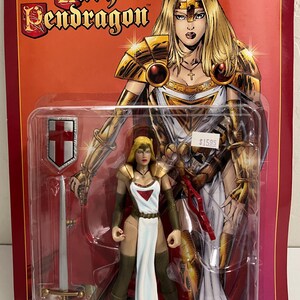 May include: A Lady Pendragon action figure in a plastic package. The figure is a blonde woman in a white and red outfit with a sword and shield. The packaging has the words "Lady Pendragon" and an illustration of the character.