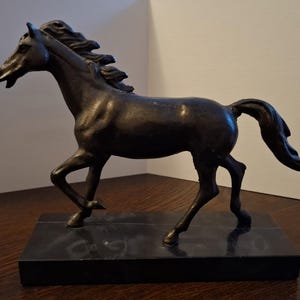 May include: A bronze-coloured sculpture of a horse in a running pose. The horse has a flowing mane and tail, and is mounted on a rectangular black base. The sculpture is detailed and appears to be made of metal.