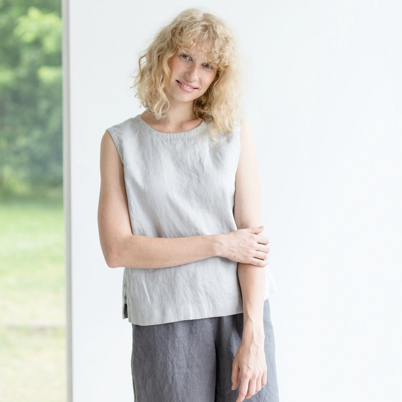May include: A woman wearing a light gray sleeveless linen top and matching gray linen pants. She is standing in front of a white wall.