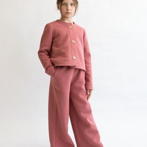 May include: A young person wearing a pink cropped jacket with buttons and matching wide-leg pants.