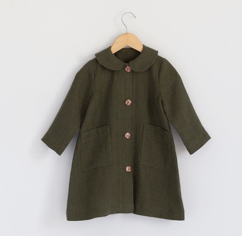 Puede incluir: Una chaqueta de lino verde con cuello de Peter Pan y bolsillos. La chaqueta tiene cinco botones en la parte delantera.