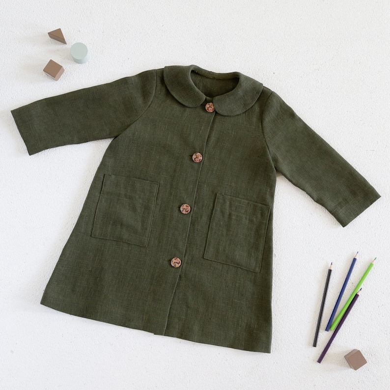 Puede incluir: Una chaqueta de lino verde con cuello de Peter Pan y botones de madera. La chaqueta tiene dos bolsillos de parche en la parte delantera.