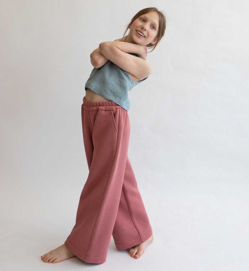 May include: A young person wearing a light blue sleeveless top and wide-legged, rose-colored pants. The pants have a drawstring waistband and pockets.