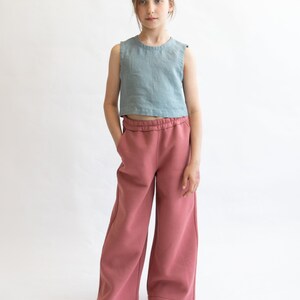 May include: A young person wearing a light blue sleeveless top and wide-legged, dusty rose pants. The pants have an elastic waistband and a relaxed fit.