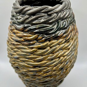 May include: A ceramic vase with a rope-like texture. The vase is glazed in shades of black, green, brown, and gold.