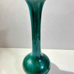 May include: A tall, slender vase with a rounded base. The vase is a deep green colour with a glossy finish.