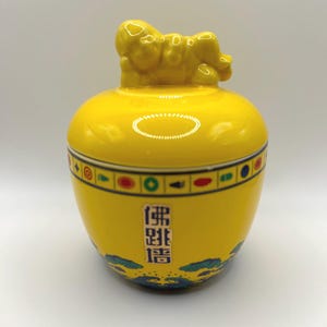 May include: A yellow ceramic jar with a lid shaped like a reclining lion. The jar has a blue and green design with Chinese characters that read "佛跳墙".