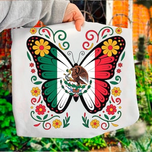 Può includere: Borsa tote bianca con un disegno a farfalla con i colori della bandiera messicana: verde, bianco e rosso. Il corpo della farfalla mostra lo stemma messicano. Il design è incorniciato da elementi floreali e a volute gialli, rossi e verdi.