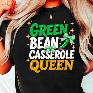 以下が含まれることがあります： 緑、白、黄色の「GREEN BEAN CASSEROLE QUEEN」の文字が入った黒いTシャツ。デザインには、グリーンビーンのさやとリボン、星のアクセントが含まれています。楽しくて食べ物をテーマにしたグラフィックTシャツです。