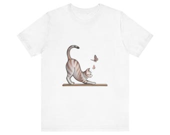 May include: White t-shirt featuring a playful illustration of a cat stretching on a wooden plank, with two butterflies fluttering nearby. The cat has brown and white stripes. The design is centered on the shirt.