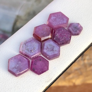 Puede incluir: Siete piedras preciosas hexagonales facetadas de color púrpura. Las piedras preciosas están dispuestas en forma escalonada, con la piedra preciosa más grande en la parte superior.