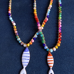 May include: Two colorful beaded necklaces with fish charms. One fish charm is blue and white, the other is orange and white.