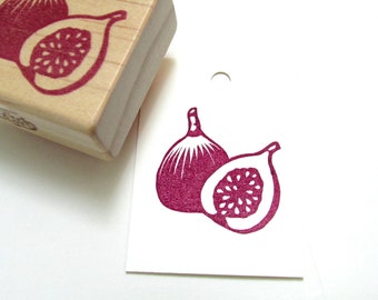 May include: A wooden fig stamp with a burgundy ink impression on white paper. The stamp shows a whole fig and a fig cut in half, revealing the seeds. The stamp is next to the fig image it creates.