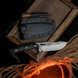 以下が含まれることがあります： 黒と灰色のポケットナイフ。黒いハンドルと銀色の刃。ナイフは、茶色の革のストラップが付いた黒い革の鞘に入っています。ナイフは木製の表面の上に置かれています。